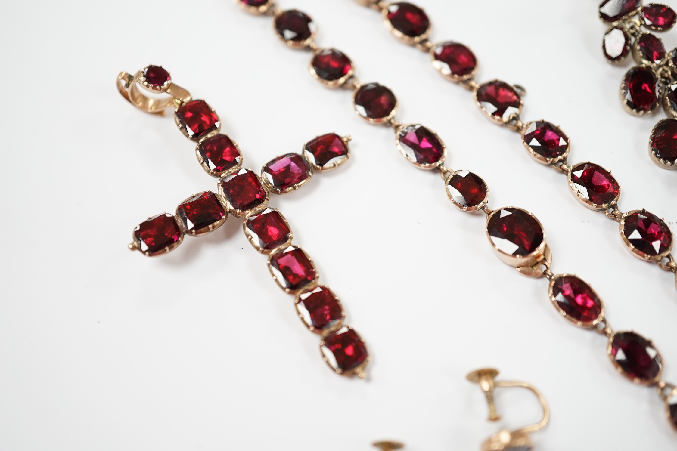 Six items of Victorian oval cut garnet set jewellery, including a yellow metal necklace (lacking drops?), 37cm, a pair of 9ct ear clips, a yellow metal cross pendant with cushion cut stones, gross weight 30 grams and a p